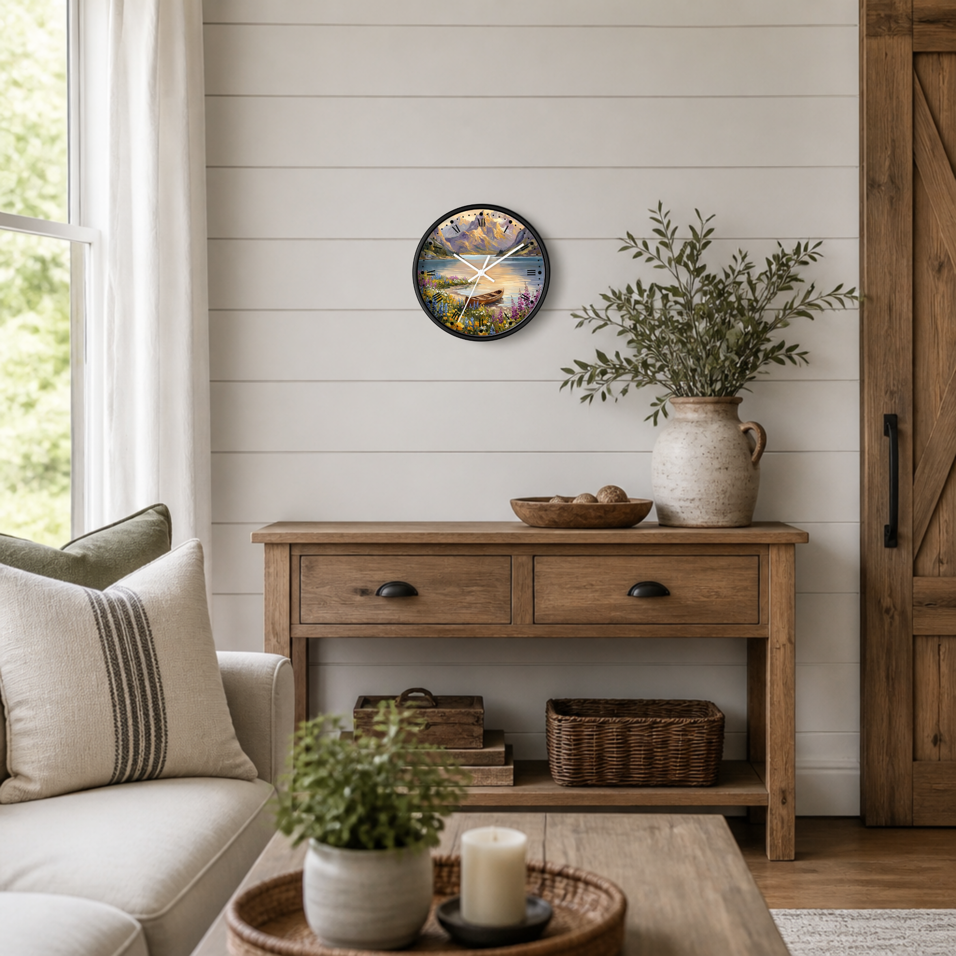 A round wall clock featuring a scenic mountain lake landscape illustration hangs on a white shiplap wall above a wooden console table in a styled living room setting.