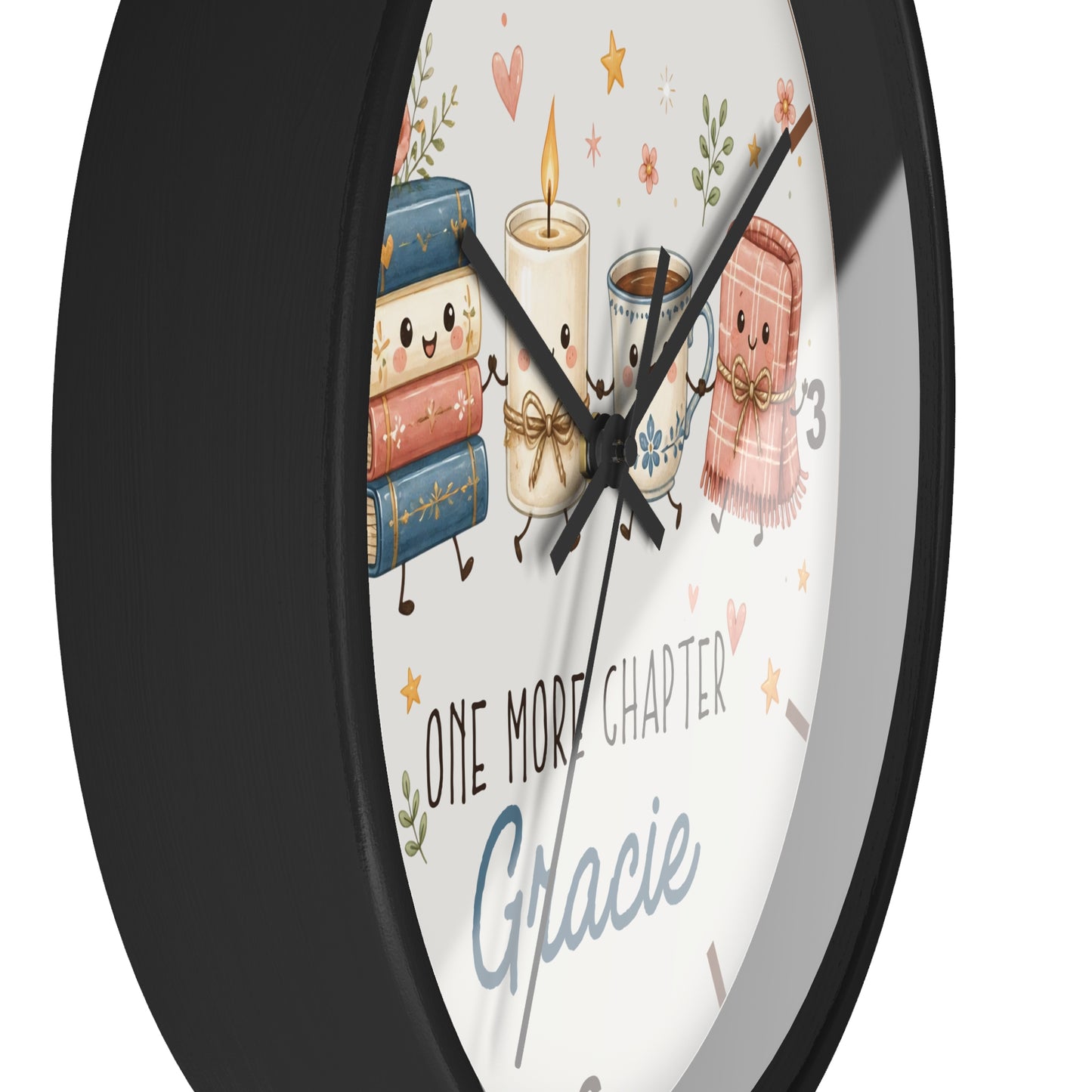 A round wall clock with a black frame and a white face featuring cute illustrations of books, a candle, a mug, and a scarf, plus the text 'ONE MORE CHAPTER Gracie'.