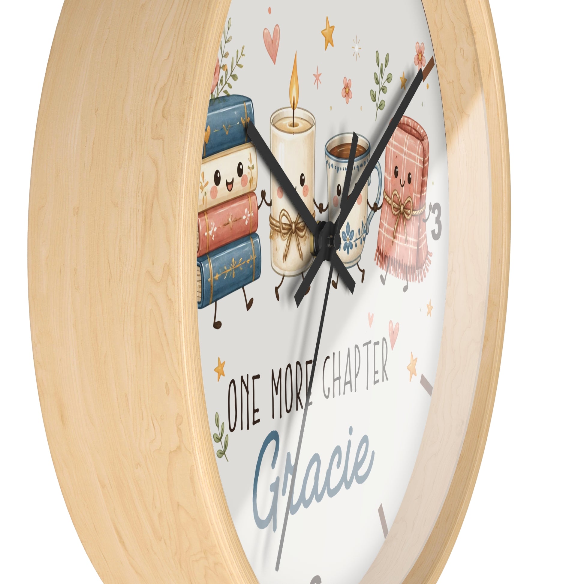 A round wall clock with a light natural wood frame and a white face featuring cute illustrated books, a candle, a mug, a scarf, and the text 'ONE MORE CHAPTER Gracie'.