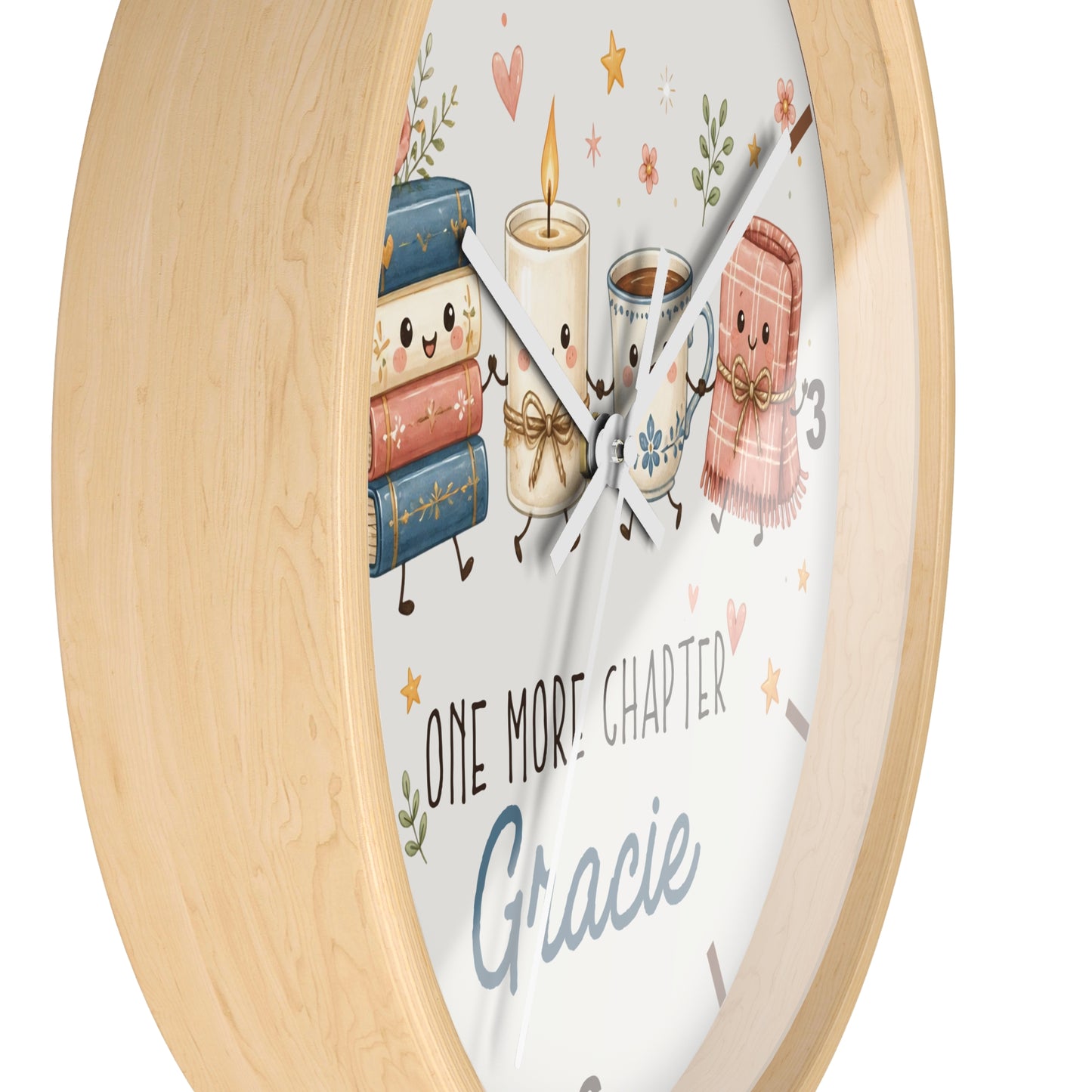 A round wall clock with a light natural wood frame and a white face featuring cute illustrated books, a candle, a mug, and a pink blanket. The clock face includes the text 'ONE MORE CHAPTER' and the name 'Gracie' in blue script.