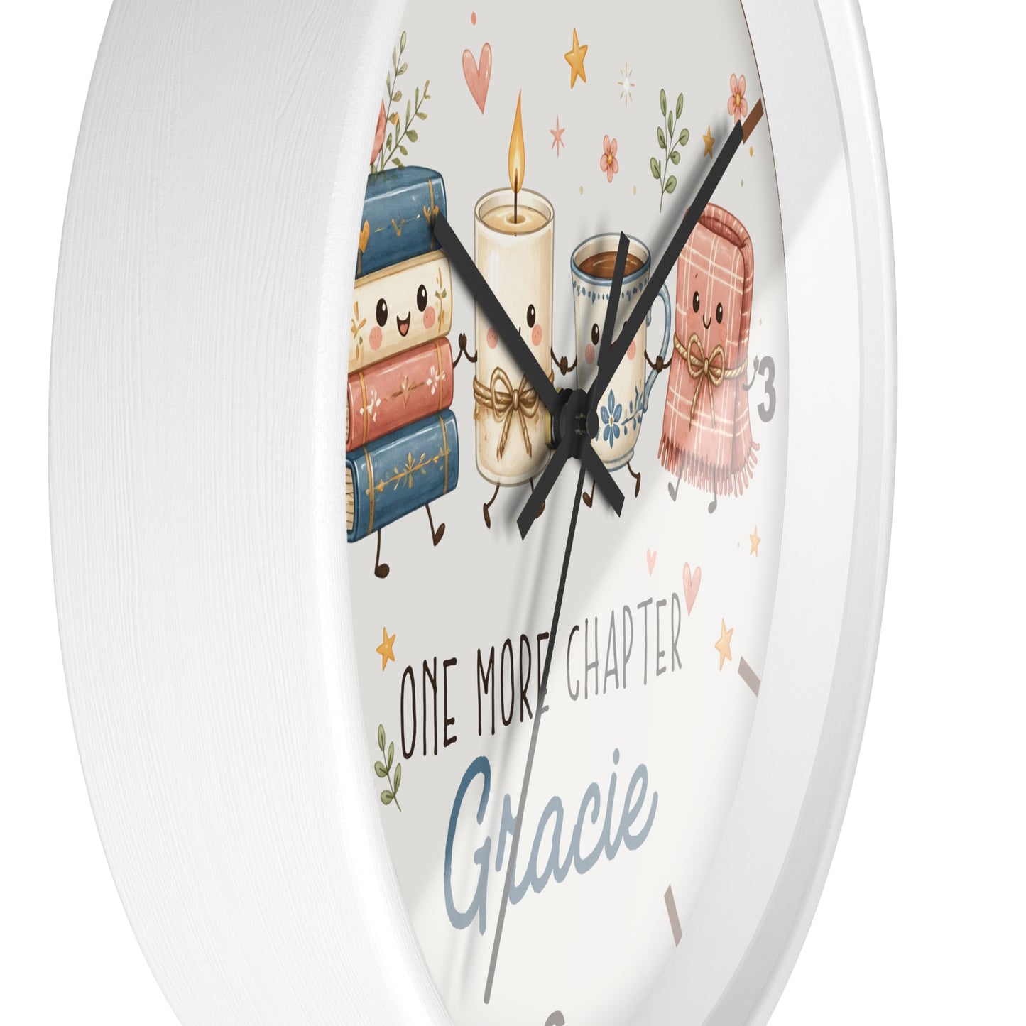 A round white wall clock with a whimsical illustration of books, a candle, a mug, and a scarf on the face, plus the text 'ONE MORE CHAPTER Gracie'.