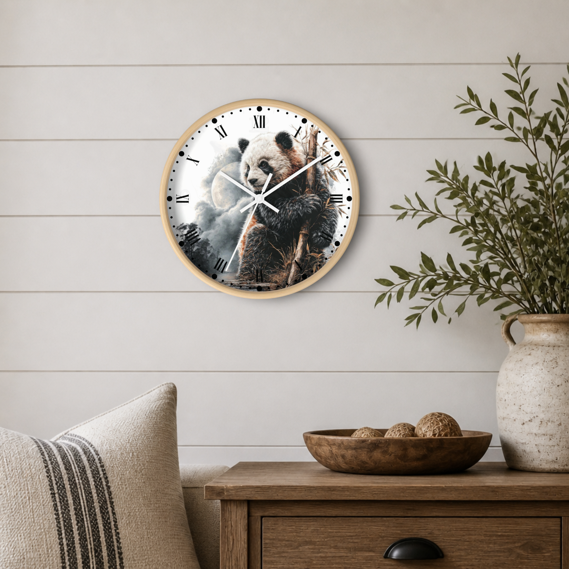 Round wall clock with a light wood frame and a printed panda illustration on the face, mounted on a white shiplap wall above a wooden side table with a plant and decorative bowl.