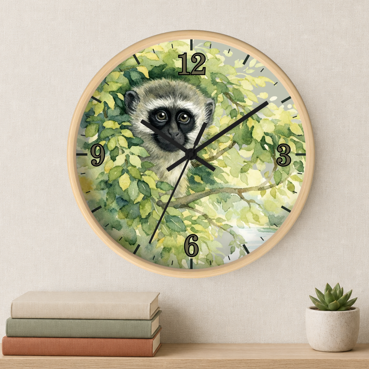 A round wall clock with a light wood frame and a printed face featuring a vervet monkey among green leaves, mounted on a beige wall above a shelf with stacked books and a small succulent.