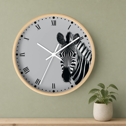 A round wall clock with a light wood frame and a gray face featuring a black-and-white zebra illustration, mounted on a sage green wall above a wooden shelf with a small potted plant.