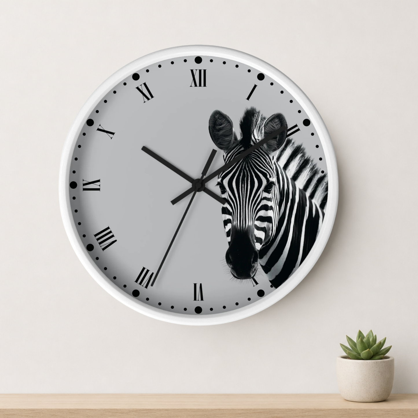 A round wall clock with a white frame and a light gray face featuring a black-and-white zebra illustration. The clock is mounted on a light beige wall above a wooden surface with a small potted succulent.