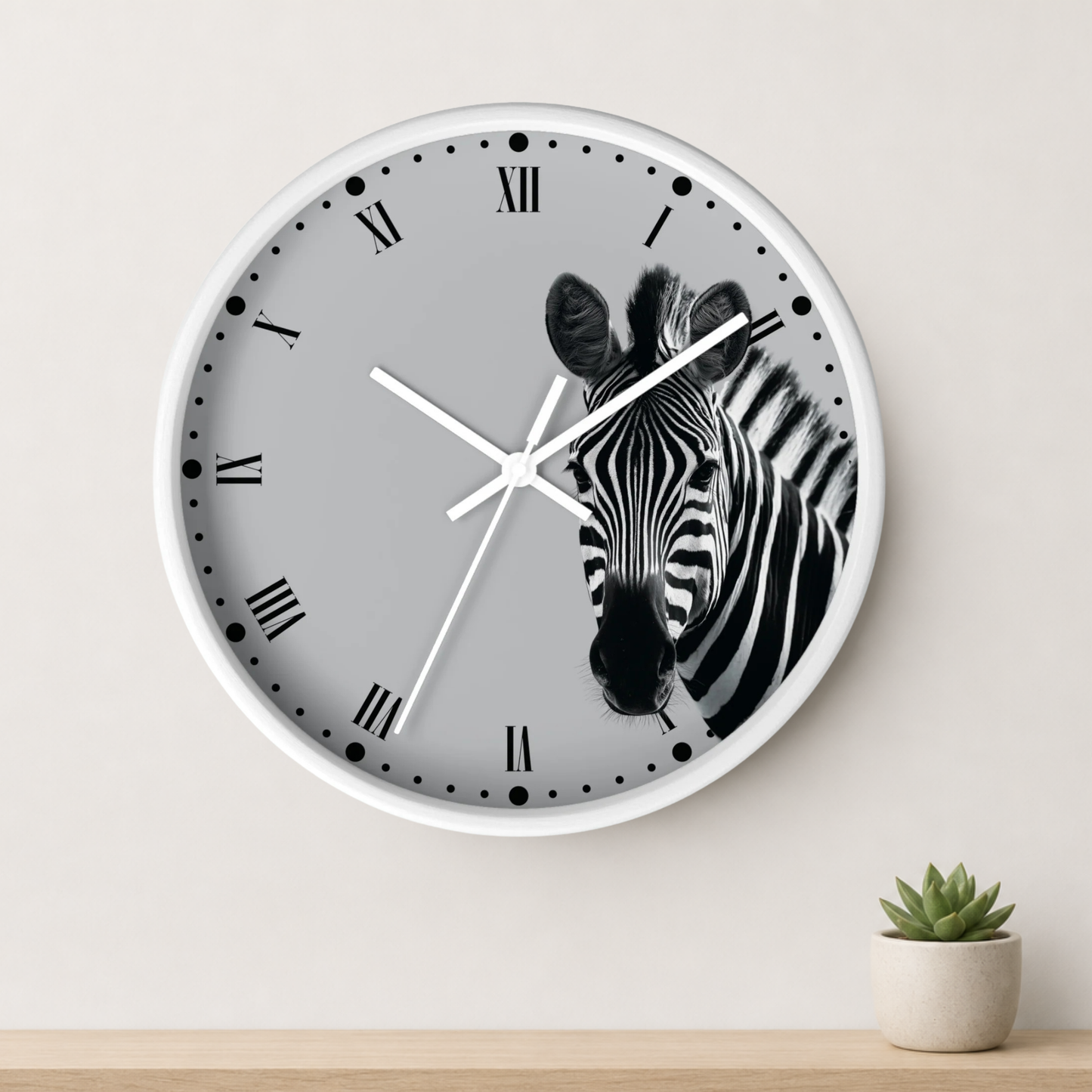 A round wall clock with a white frame and a gray face featuring a black-and-white zebra illustration, mounted on a light wall above a small potted succulent.