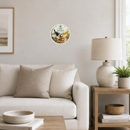 A round wall clock with a golden sun and moon illustration hangs on a light gray wall above a beige sofa in a styled living room setting.