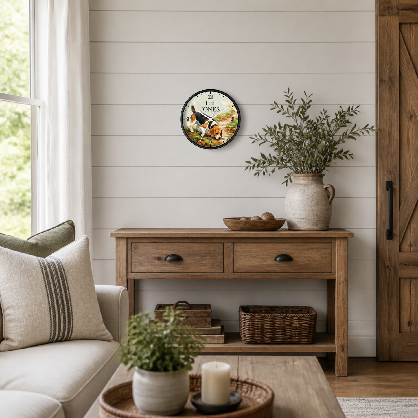A round wall clock with a rustic black frame and colorful autumn-themed dog illustration hangs on a white shiplap wall above a wooden console table in a bright, modern farmhouse-style living room.