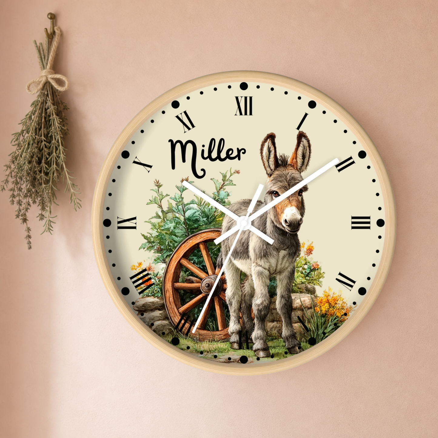 Personalized round wall clock featuring a donkey illustration, a rustic wagon wheel, and the name 'Miller' in script on a cream dial with black Roman numerals, mounted on a warm beige wall with dried herbs hanging to the left.