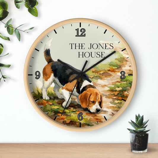 A round wooden wall clock with a custom printed illustration of a beagle dog and the text 'THE JONES HOUSE' on the clock face, styled on a wooden shelf against a white wall with small plants.