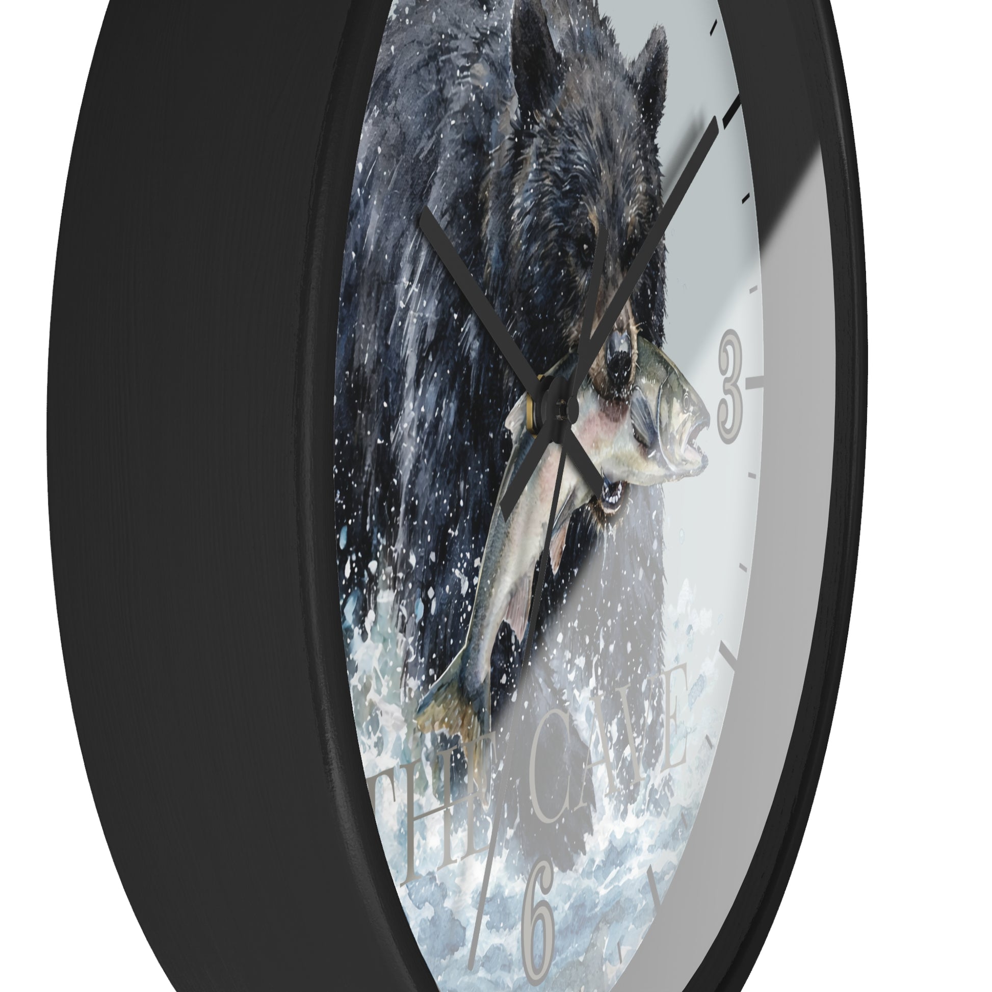 A round wall clock with a black frame and a printed face showing a black bear catching a fish in splashing water. The clock is shown at an angle against a plain white background.