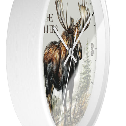 Round wall clock with a white frame and a printed moose illustration on the face, with partial text reading 'THE MILLLERS' and clock numbers visible.