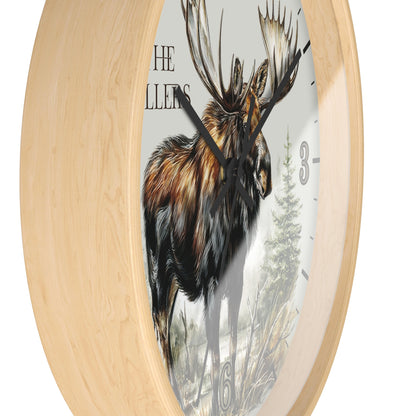 Round wall clock with a light natural wood frame and a printed face featuring a moose illustration, partial text reading 'THE MILLERS', and black clock hands.