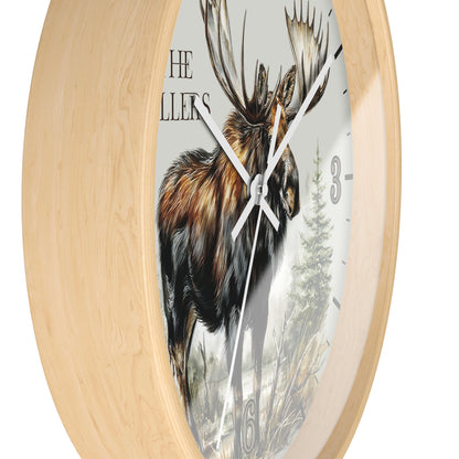 Round wall clock with a light natural wood frame and a printed face featuring a moose illustration, partial text, and black hour markers.