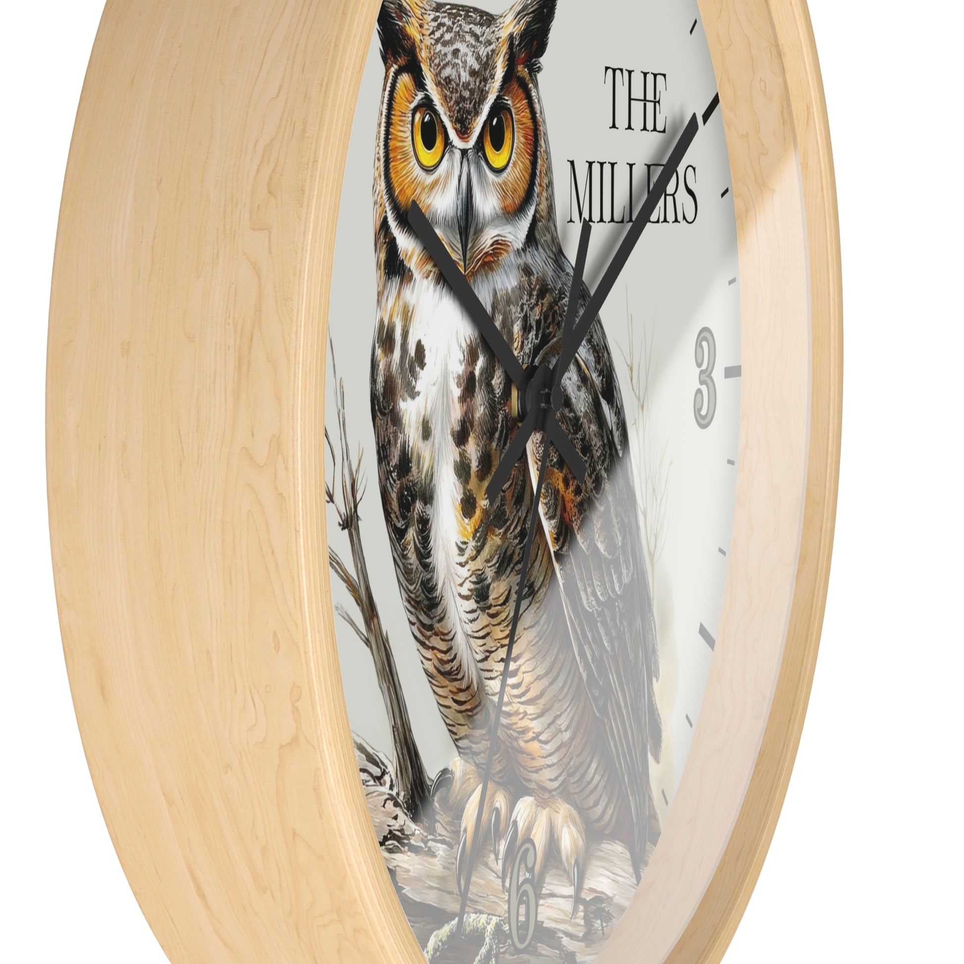 Round wall clock with a light natural wood frame and a white dial featuring a large owl illustration and the text 'THE MILLERS'.