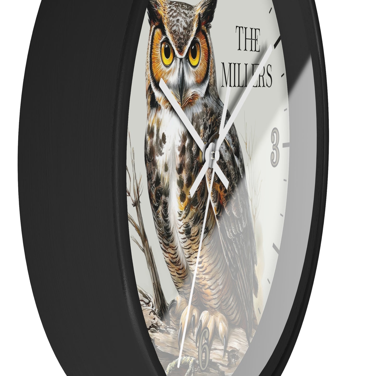 A round wall clock with a black frame and a white face featuring a detailed illustration of a great horned owl. The text 'THE MILLERS' is printed on the clock face, along with black Arabic numerals.