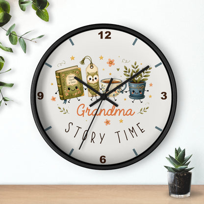 A round wall clock with a black frame and a white face, featuring a whimsical 'Grandma Story Time' illustration with cartoon characters, a book, a mug, and potted plants. The clock is shown hanging on a white wall above a wooden shelf with small green plants.