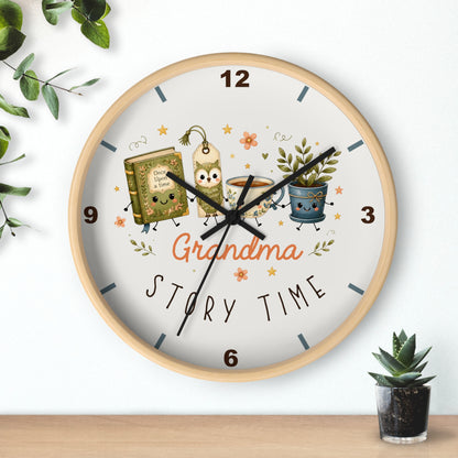 A round wall clock with a light wood frame and a white face, decorated with cartoon illustrations of a book, a candle, a coffee cup, and a potted plant, with the words 'Grandma Story Time' in the center. The clock is mounted on a white wall above a wooden shelf with small green plants.