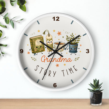 A round wall clock with a white face and silver rim, featuring a whimsical 'Grandma Story Time' illustration with a book, mug, and potted plant. The clock is mounted on a white wall above a wooden shelf with small green plants.