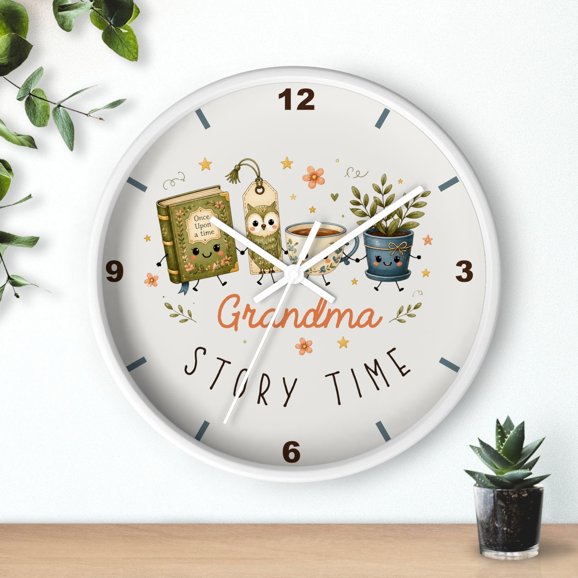 A round wall clock with a white frame and a whimsical 'Grandma Story Time' illustration on the dial, styled on a light wall above a wooden surface with small potted plants.