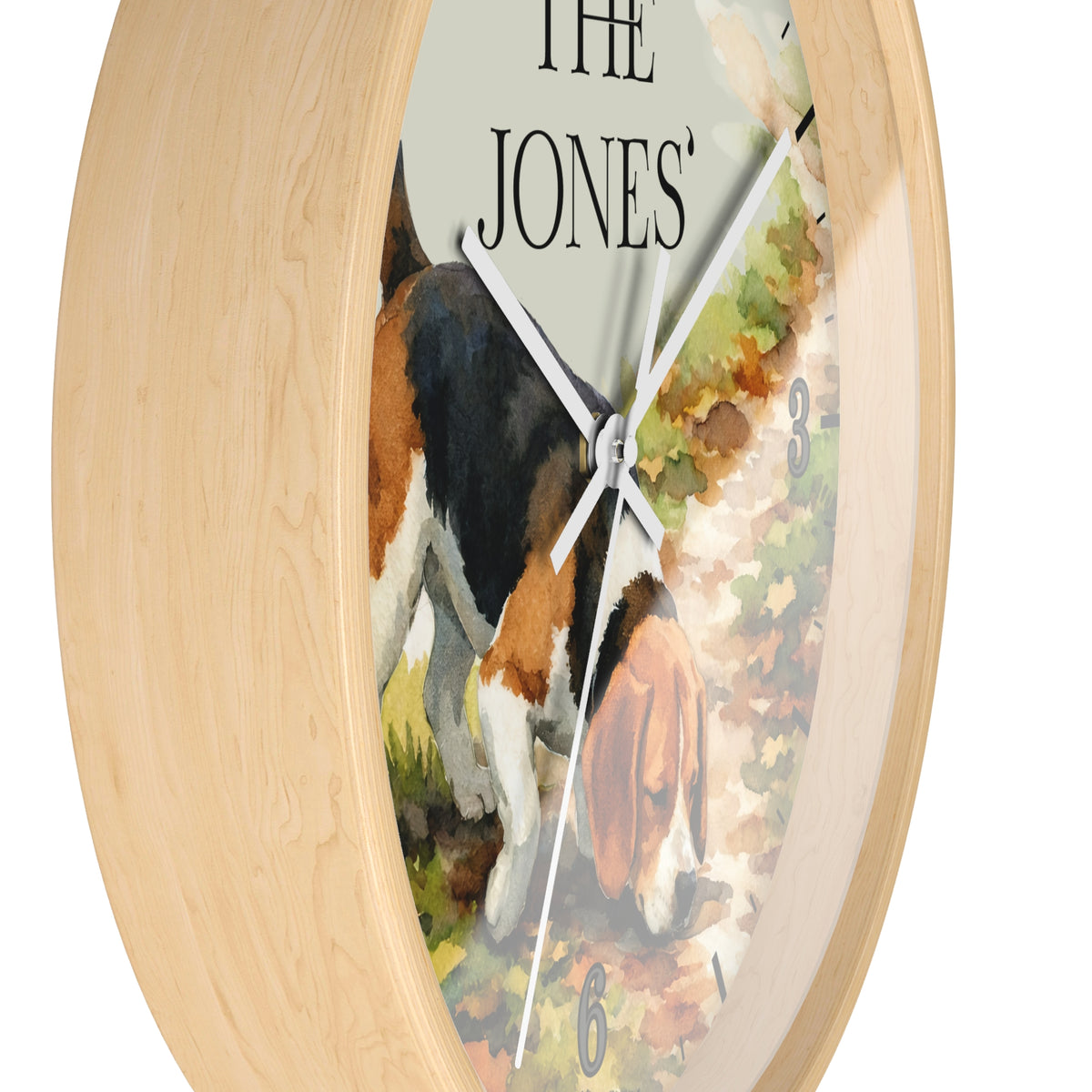 Round wall clock with a light natural wood frame and a printed dog illustration on the face. The clock shows the text 'THE JONES' at the top and has white hands against a mostly off-white dial with a watercolor-style dog scene in black, tan, brown, and green tones.