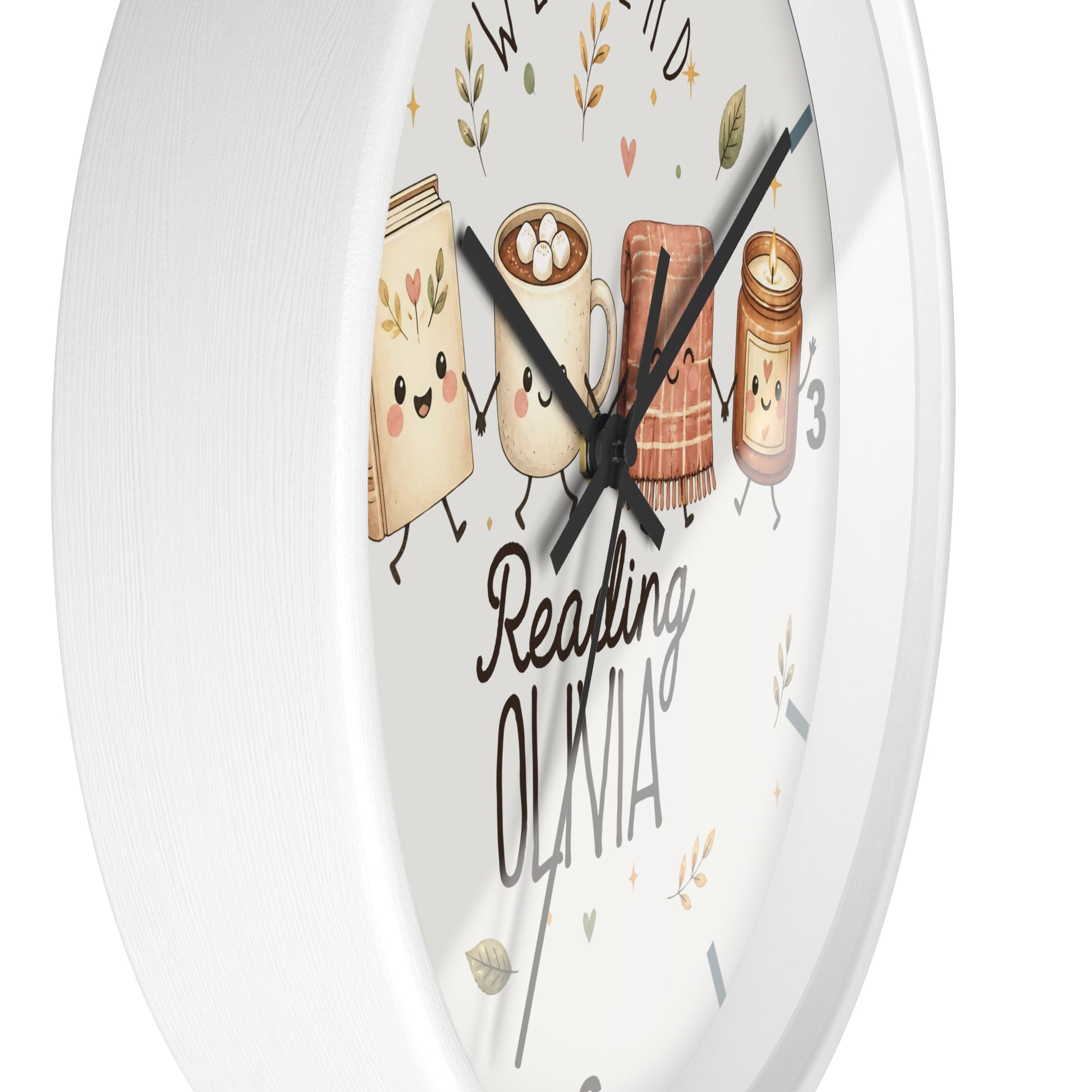 A round white wall clock with a whimsical reading-themed face. The clock face features cute illustrations of a book, a mug with marshmallows, a cozy blanket, and a candle, along with the text 'Reading OLIVIA' in black script and block lettering.
