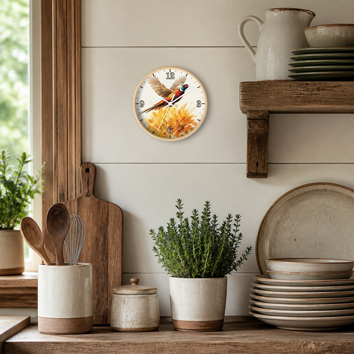 A round wall clock featuring a pheasant bird perched on yellow flowers, mounted on a white shiplap wall in a rustic kitchen setting with wooden shelves, ceramic dishes, and potted plants.