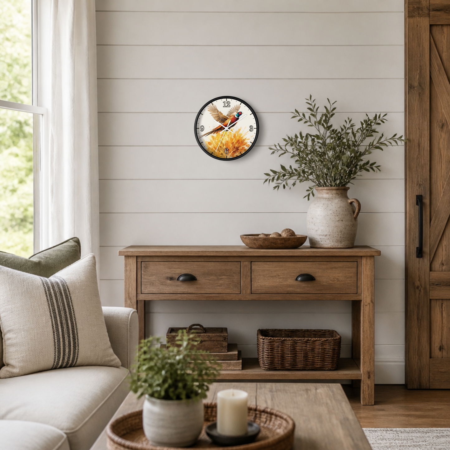 A round wall clock featuring a bird perched on a stalk of wheat, styled in a rustic living room above a wooden console table.