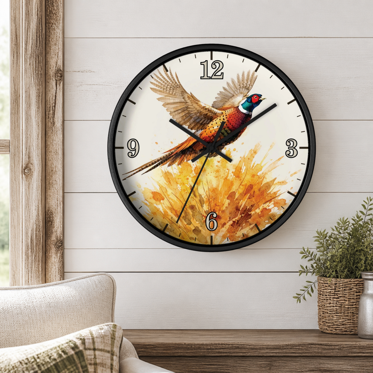 A round wall clock with a black frame hangs on a white shiplap wall above a wooden console table. The clock face features a colorful pheasant bird in flight over a golden floral burst.