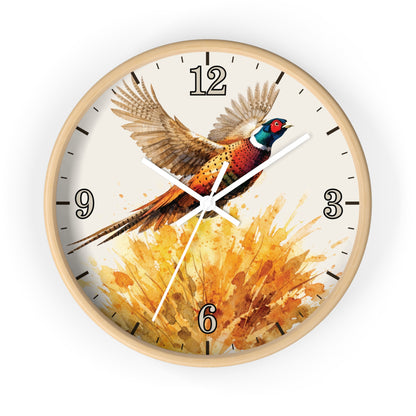 A round wall clock with a light natural wood frame and a printed bird illustration on the face. The design shows a pheasant in flight above a warm orange and yellow watercolor splash, with black Arabic numerals and black hour markers.