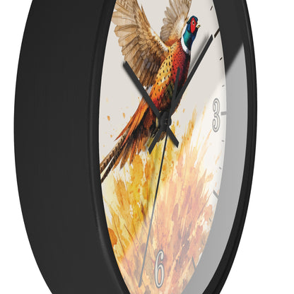 A round wall clock with a black frame and a printed face featuring a pheasant bird in flight over a warm yellow and orange watercolor background. The clock is shown at an angle against a plain white background.