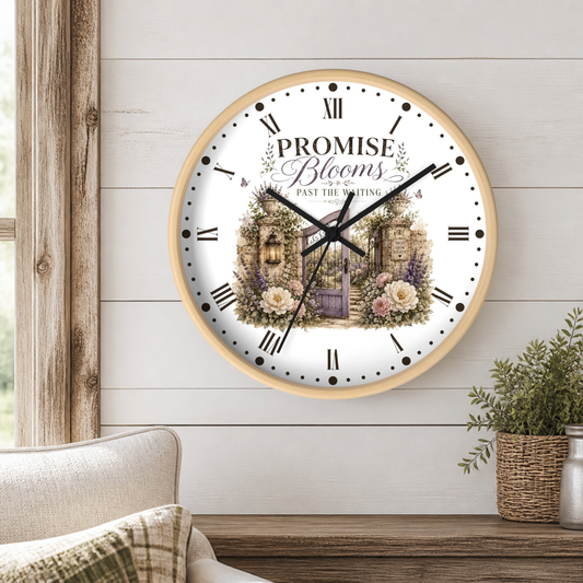 A round wall clock with a light wood frame hangs on a white shiplap wall above a wooden table. The clock face features a white background with black Roman numerals, black hands, and a central illustration of a purple gate, lavender, and white flowers, with the text 'PROMISE Blooms Past the Waiting.