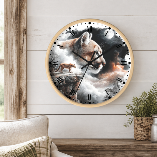 A round wall clock with a light wood frame hangs on a white shiplap wall above a wooden mantel. The clock face features a surreal printed design with a large mountain lion head, a smaller lion cub on a rock, clouds, and a full moon.