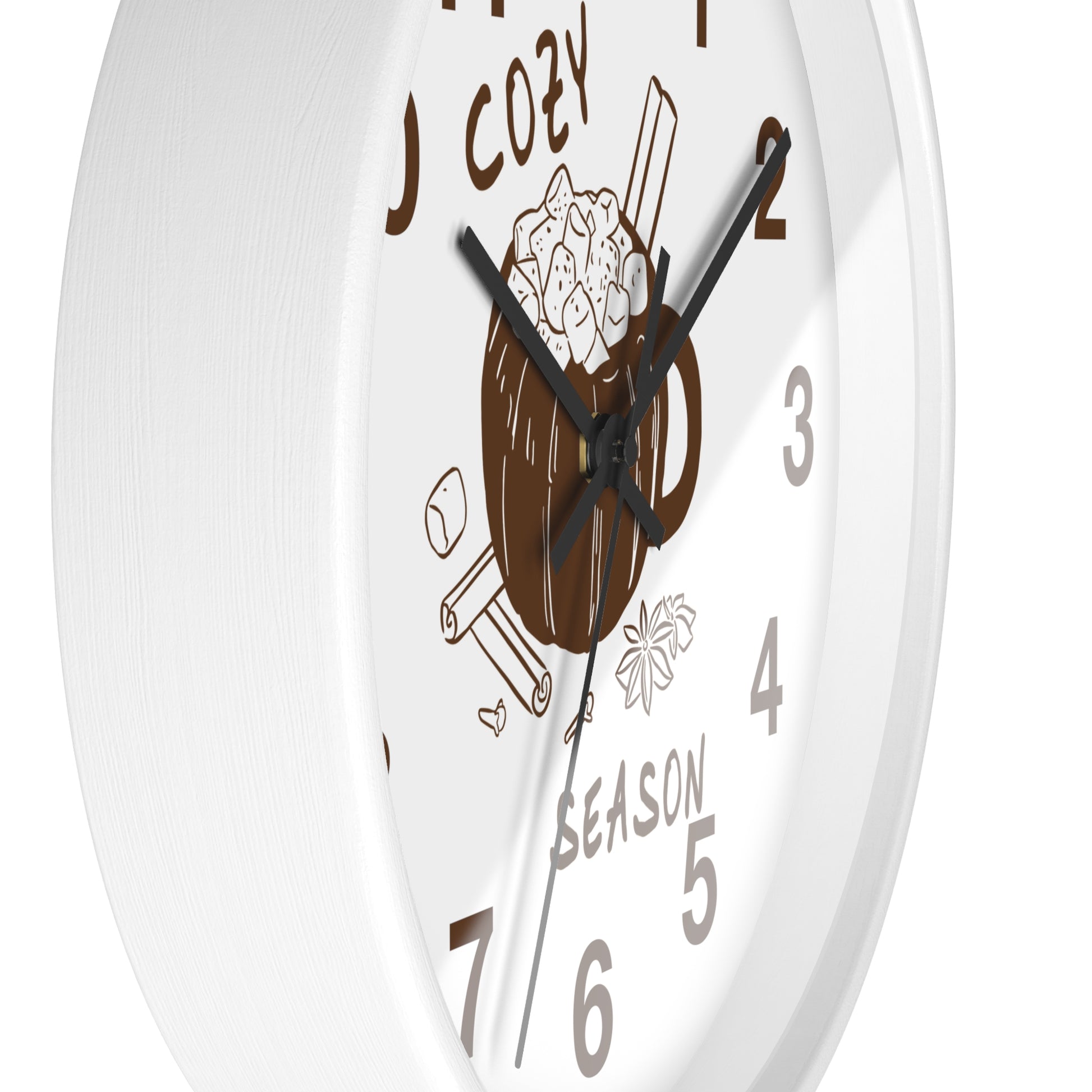 A white round wall clock with a cozy coffee-themed illustration on the face, including a mug, cinnamon sticks, marshmallows, and the words 'COZY' and 'SEASON'.