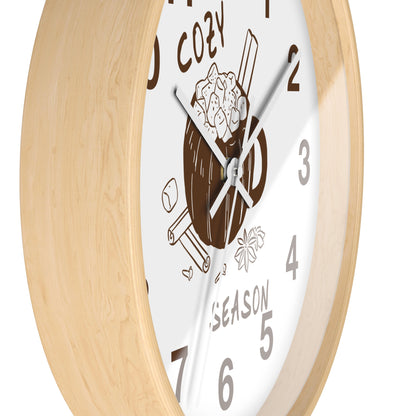 A close-up of a round wall clock with a light natural wood frame and a white face featuring a brown mug illustration and gray numerals.