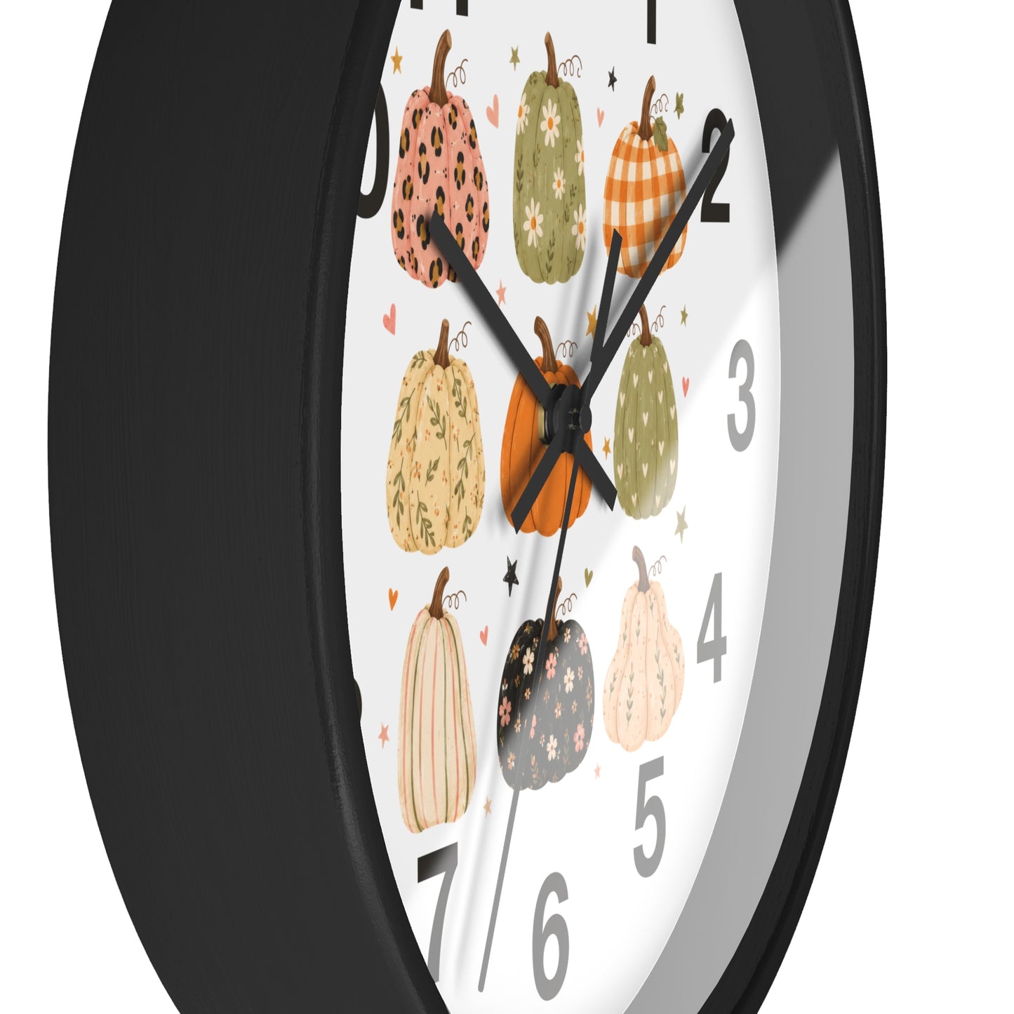 A close-up of a round wall clock with a black frame and a white face decorated with illustrated pumpkins in autumn colors, including orange, green, beige, and black patterns.