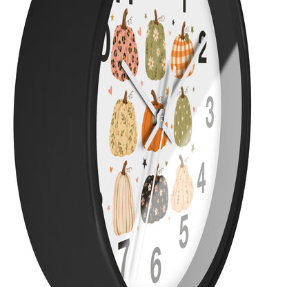 A close-up of a round wall clock with a black frame and a white face decorated with illustrated patterned pumpkins and gray Arabic numerals.