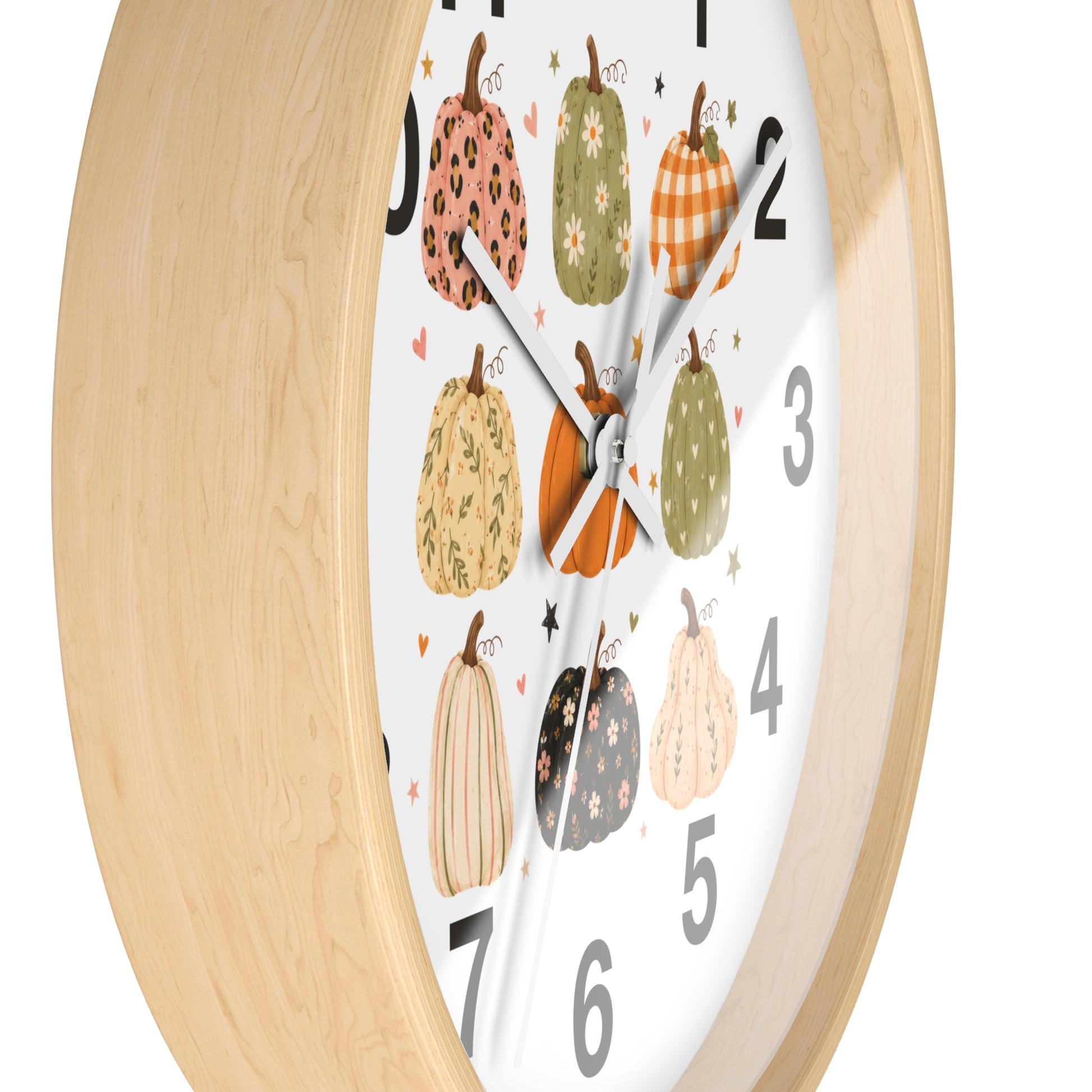 A close-up of a wall clock with a light natural wood frame and a white face decorated with illustrated pumpkins in autumn colors and large black numerals.