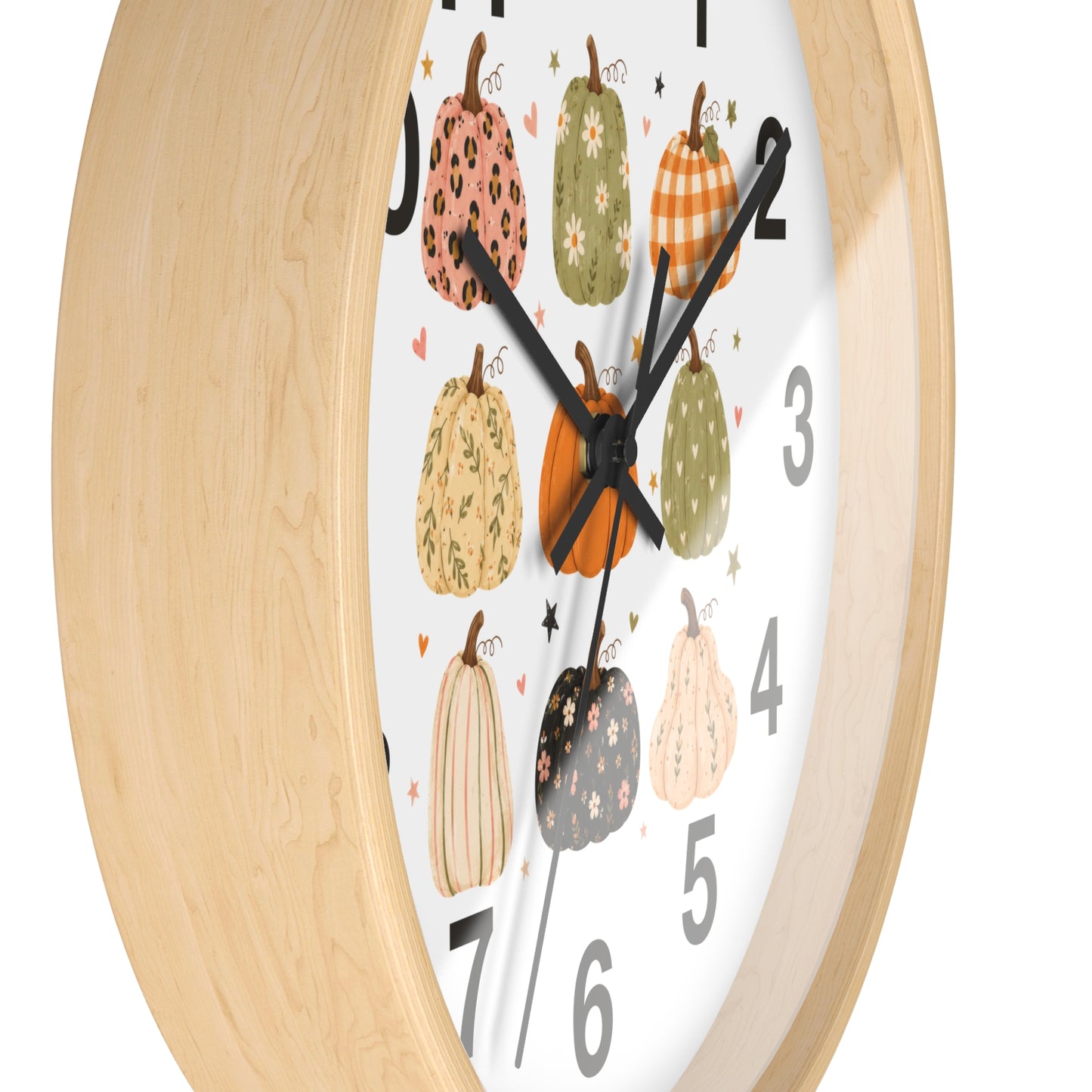 A close-up of a round wall clock with a light natural wood frame and a white face decorated with illustrated pumpkins in autumn colors and black numerals.