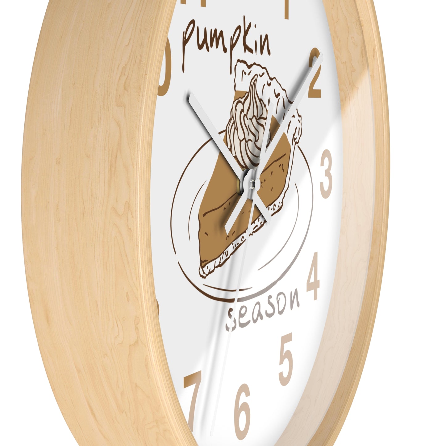 A close-up of a round wall clock with a light natural wood frame and a white face featuring a pumpkin pie illustration and the words 'pumpkin season.'.