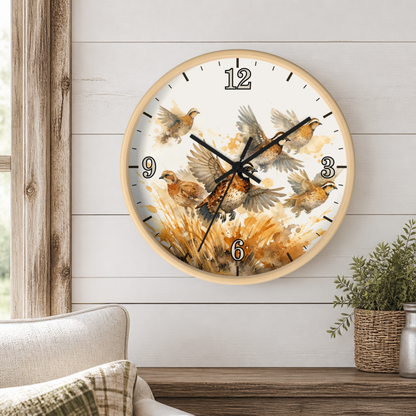 A round wall clock with a light wood frame and a watercolor-style bird illustration, mounted on a white shiplap wall above a wooden table with a potted plant and part of a sofa visible.