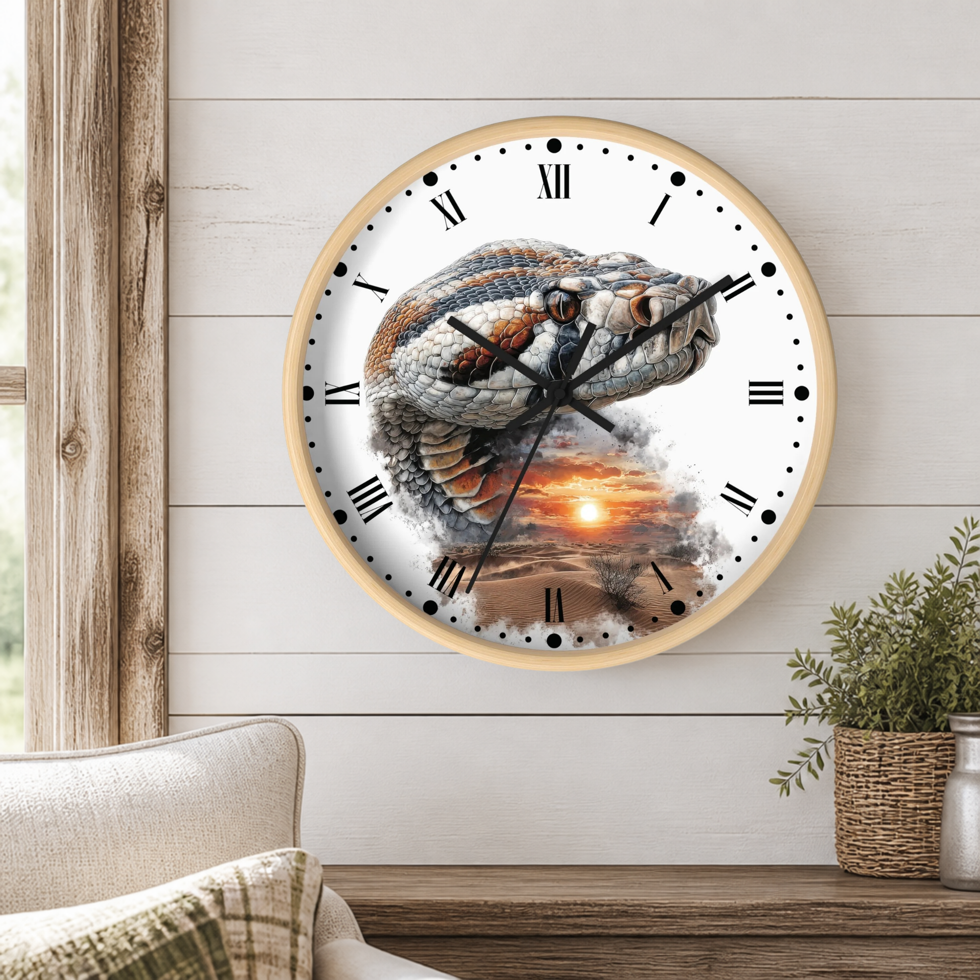 A round wall clock with a light wood frame and a printed design of a coiled snake over a sunset landscape. The clock is mounted on a white shiplap wall above a wooden console table, with a beige sofa and a small potted plant visible in the room setting.