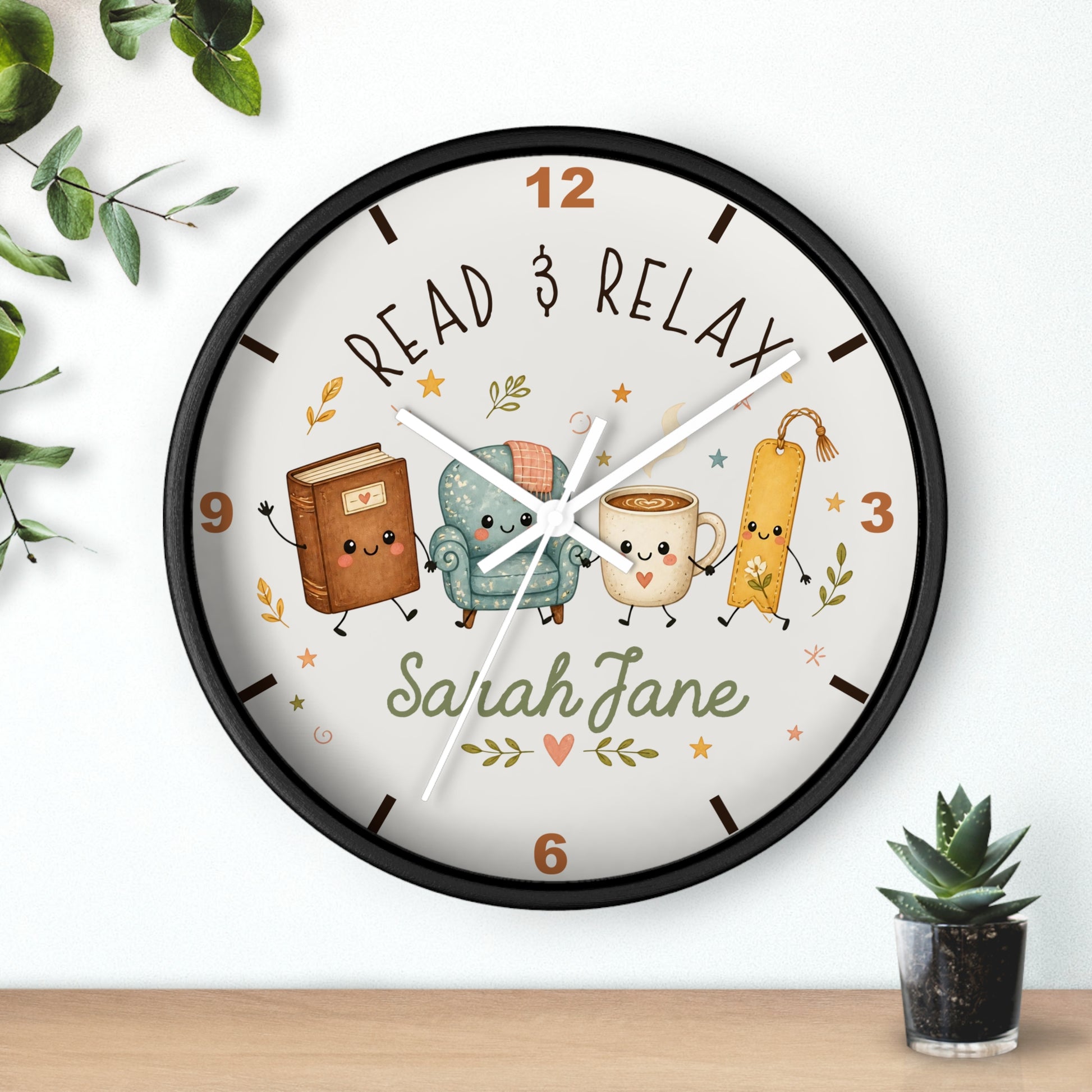 A personalized round wall clock with a black frame and a whimsical reading-themed dial. The clock face features cute illustrations of a book, a cozy armchair, a smiling mug, and a bookmark, surrounded by the words 'READ & RELAX' and the custom name 'Sarah Jane'.