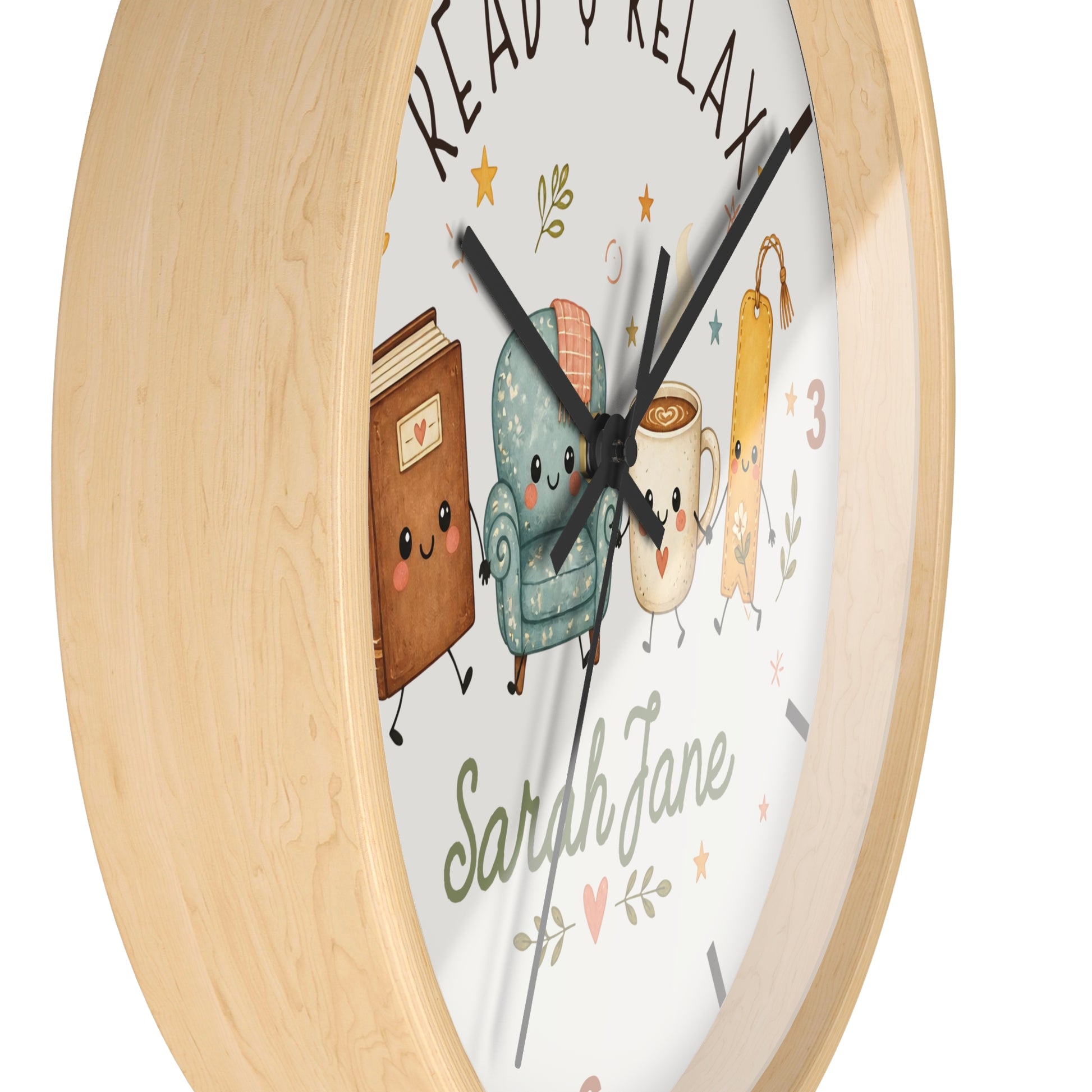 A round wall clock with a light natural wood frame and a white face featuring cute cartoon illustrations of a book, armchair, mug, and key, with the words 'READ & RELAX' and the name 'Sarah Jane'.