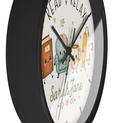 A round wall clock with a black frame and a white face featuring cute illustrated characters: a brown book, a teal armchair, a mug, and a book tag. The words 'READ & RELAX' appear at the top, and 'Sarah Jane' is written at the bottom.