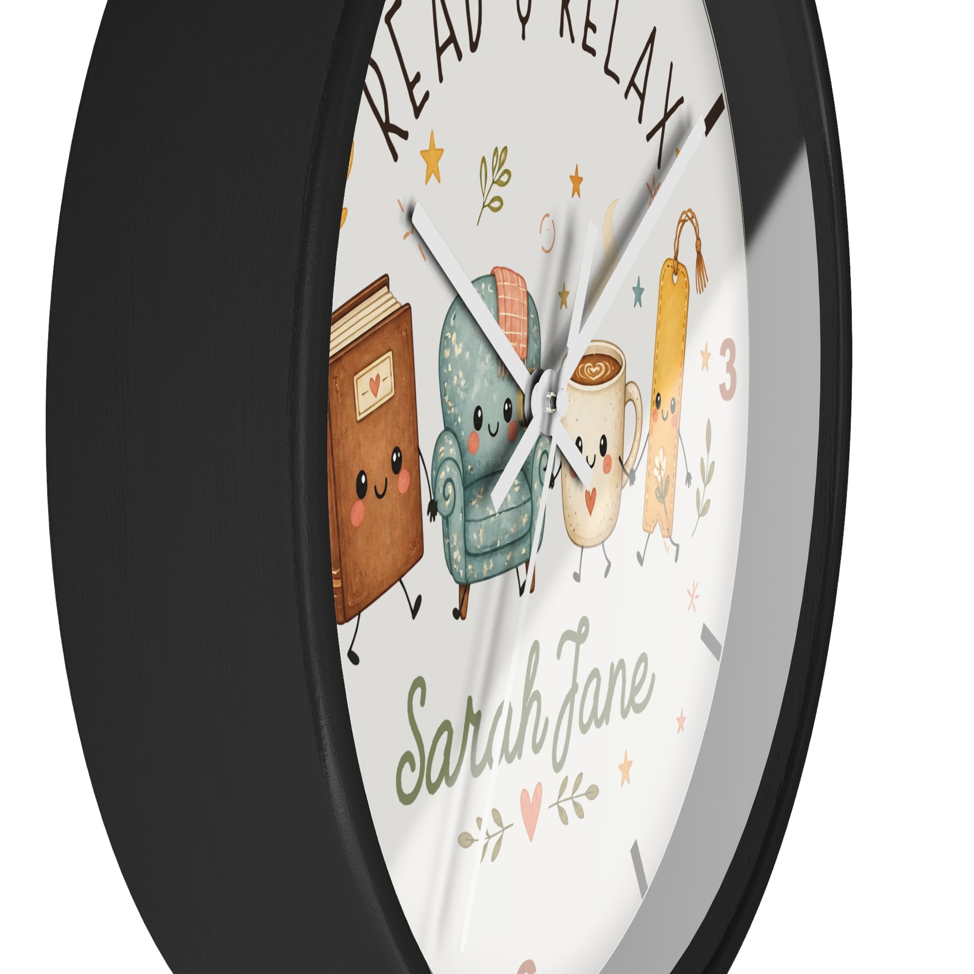 A round wall clock with a black frame and a white face featuring a cute illustration of a book, armchair, mug, and book keychain, with the words 'READ & RELAX' and the name 'Sarah Jane' written on it.