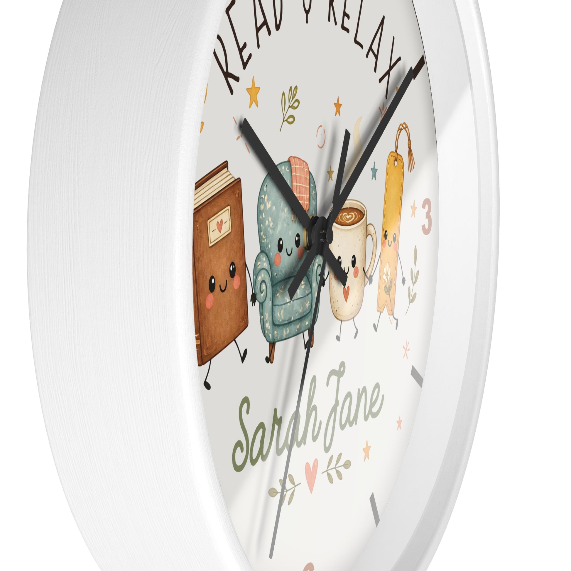 A round white wall clock with a whimsical cartoon illustration of a book, armchair, mug, and coffee cup on the face. The words 'READ & RELAX' appear at the top, and the name 'Sarah Jane' is written in script near the bottom.