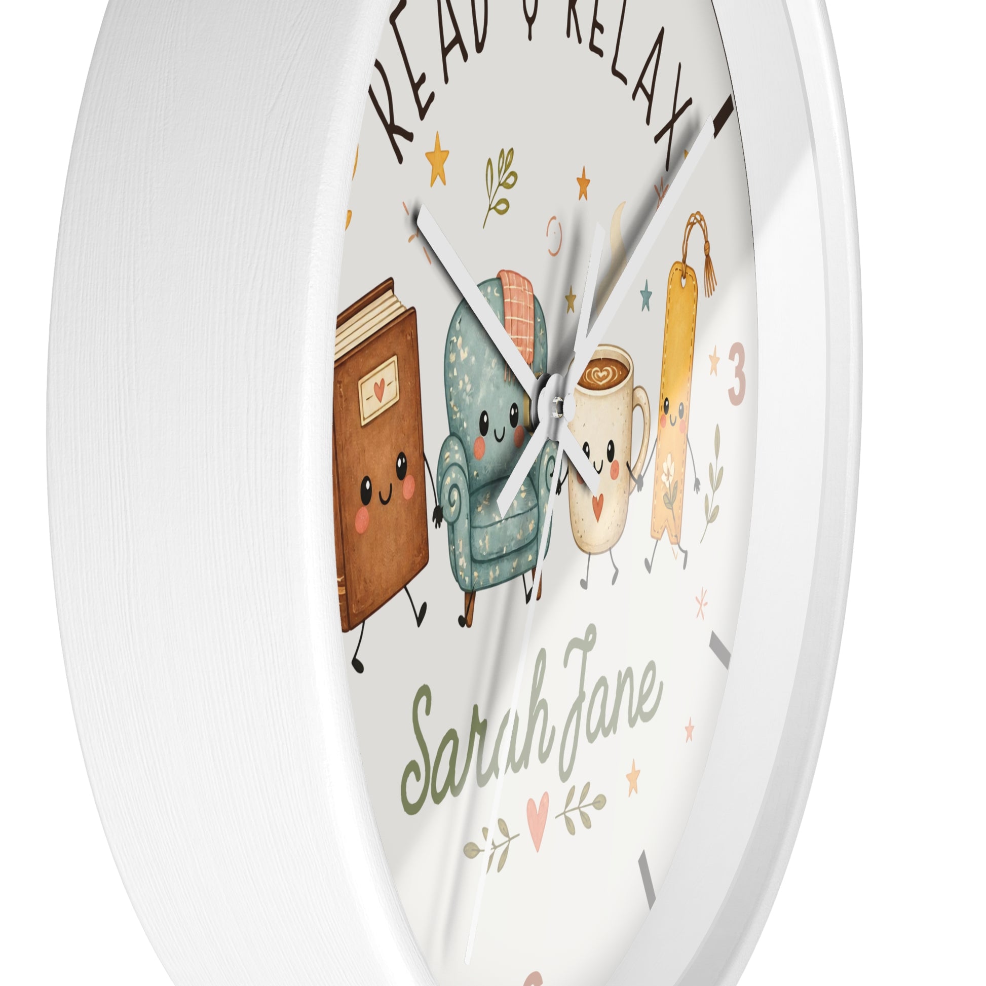 A round white wall clock with a whimsical illustration of a book, armchair, mug, and coffee cup on the face, along with the words 'READ & RELAX' and the customizable name 'Sarah Jane'.