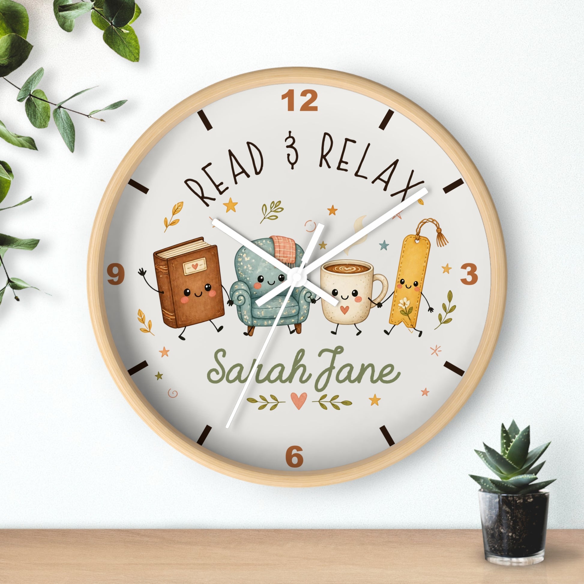 A round personalized wall clock with a light wood frame, featuring a white face with the text 'READ & RELAX' and the name 'Sarah Jane'. The clock face is decorated with cute illustrations of a book, a teal armchair, a mug, and a bookmark.