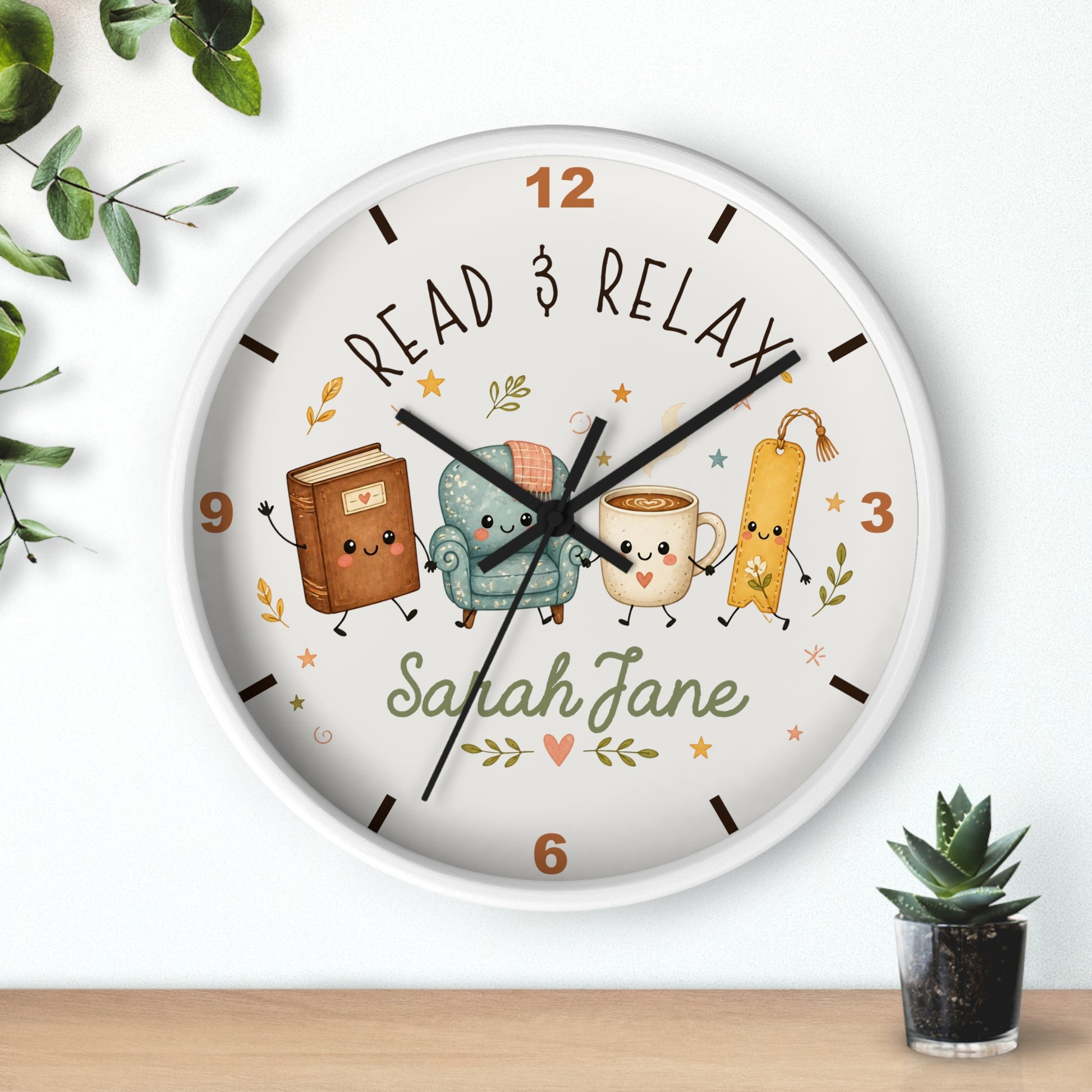 A round wall clock with a white frame and a whimsical book-themed dial. The clock face features the text 'READ & RELAX' and the personalized name 'Sarah Jane' in green script, surrounded by cute illustrations of a brown book, a teal armchair, a yellow mug, and a bookmark.